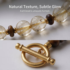 Macro close-up of natural golden crystal beads and polished gold titanium steel clasp, highlighting unique natural textures and subtle internal glow.