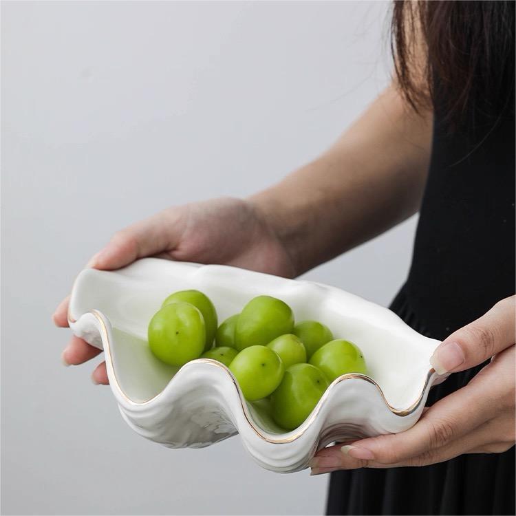 Handheld white shell craft product bowl with organic shell shape and gold edge, ideal for serving small snacks or decorative use.