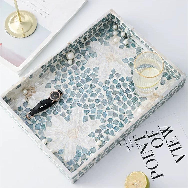 Rectangular seashell tray displaying a small conch shell and a sand dollar, ocean themed interior styling.