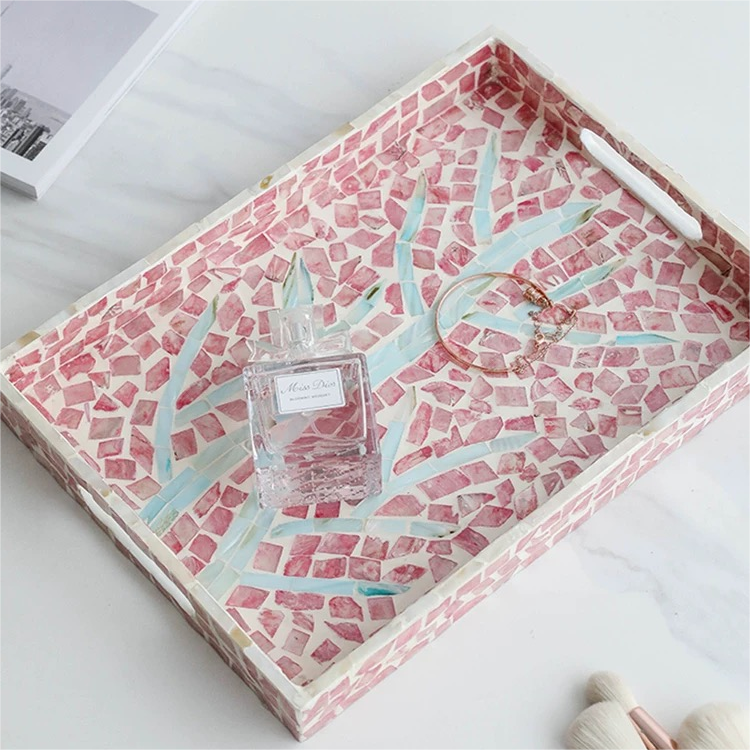 Seashell craft tray placed on a wooden nightstand beside a lamp and an alarm clock, holding eyeglasses.